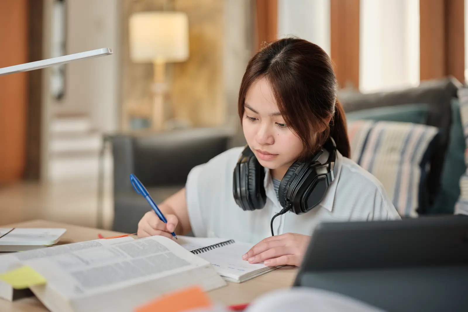 A student writing at a desk with notes and a tablet